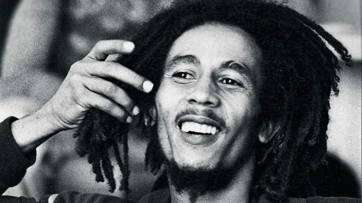 Portrait en noir et blanc de Bob Marley souriant, la main près de ses dreadlocks Imagen