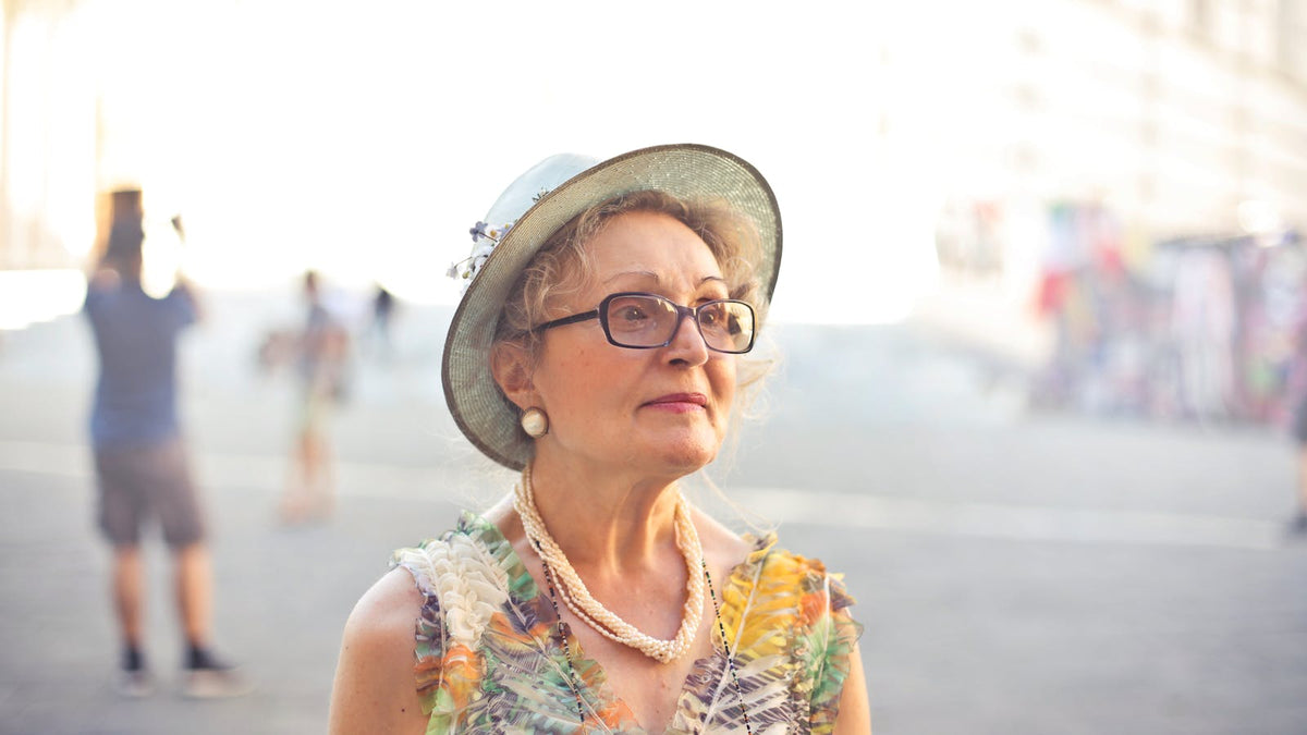 Femme de plus de 60 ans portant lunettes, rouge à lèvres rose, chapeau et collier perlé Imagen