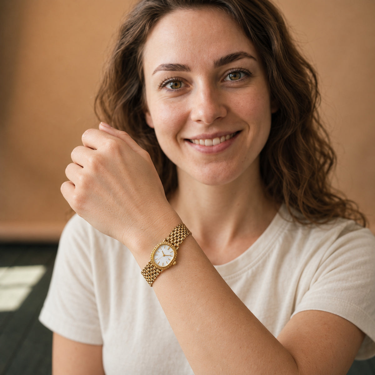 Montre vintage femme à bracelet maille or et cadran blanc portée au poignet sur un chemisier blanc, vue en studio Imagen