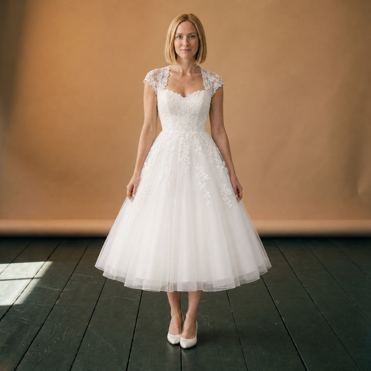 Robe de mariée courte en dentelle et tulle portée en studio, vue en pied de face Imagen
