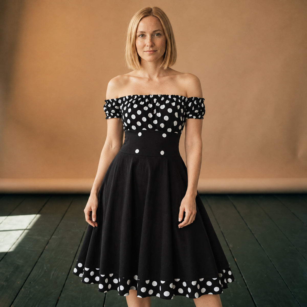 Robe vintage années 60 noire à pois blancs portée en studio, épaules dénudées, vue de face Imagen